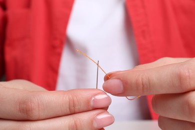 Woman inserting thread through eye of needle, closeup