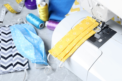 Photo of Sewing machine, homemade protective masks and craft accessories on grey marble table