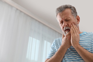 Photo of Mature man suffering from strong tooth pain at home, space for text