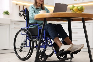 Woman in wheelchair using laptop at table in home office, closeup