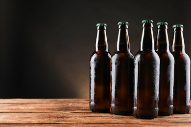 Many bottles of beer on wooden table against dark background, space for text