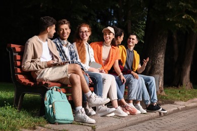 Photo of Group of happy students spending time together on bench in park