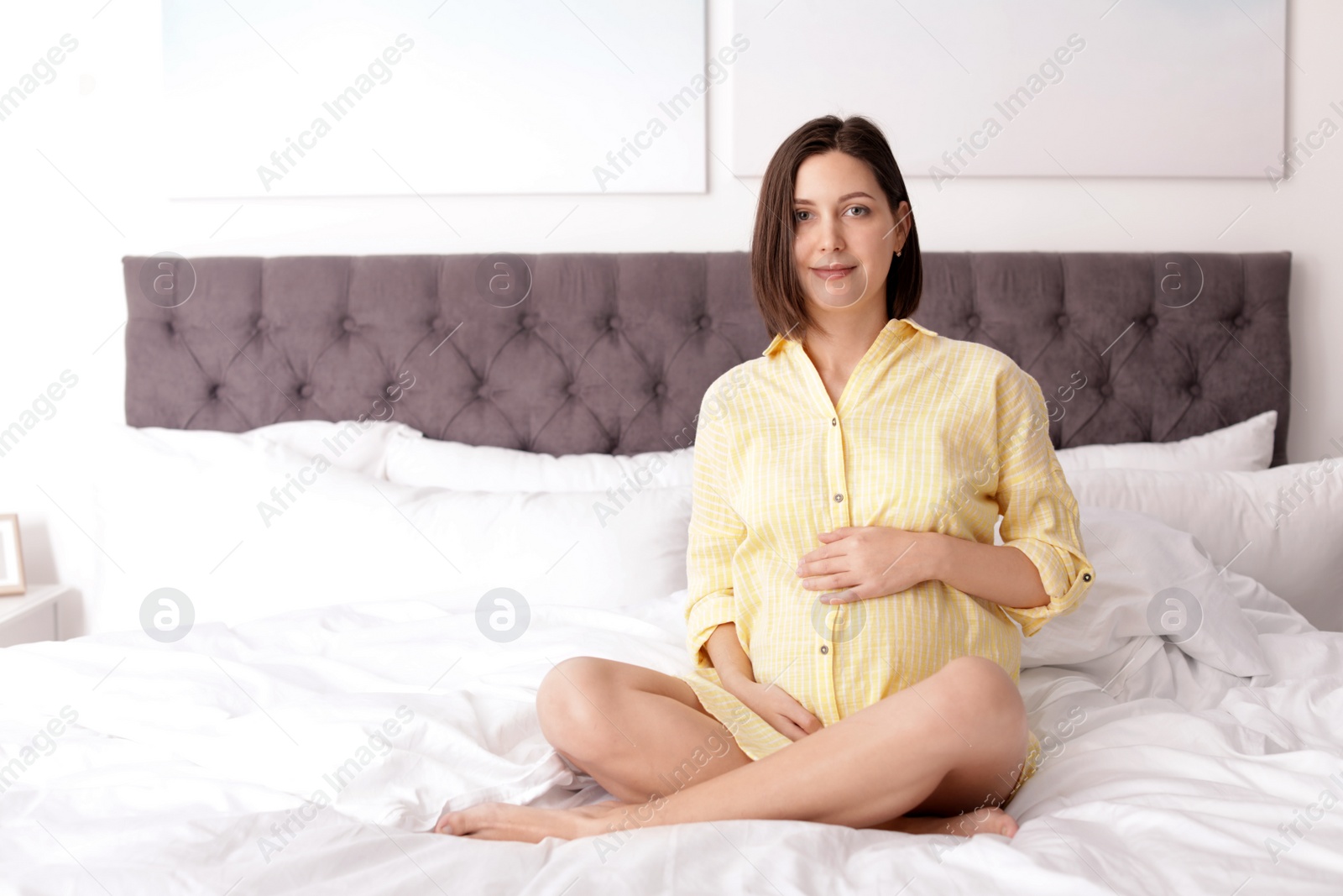 Photo of Beautiful pregnant woman sitting on bed at home. Space for text