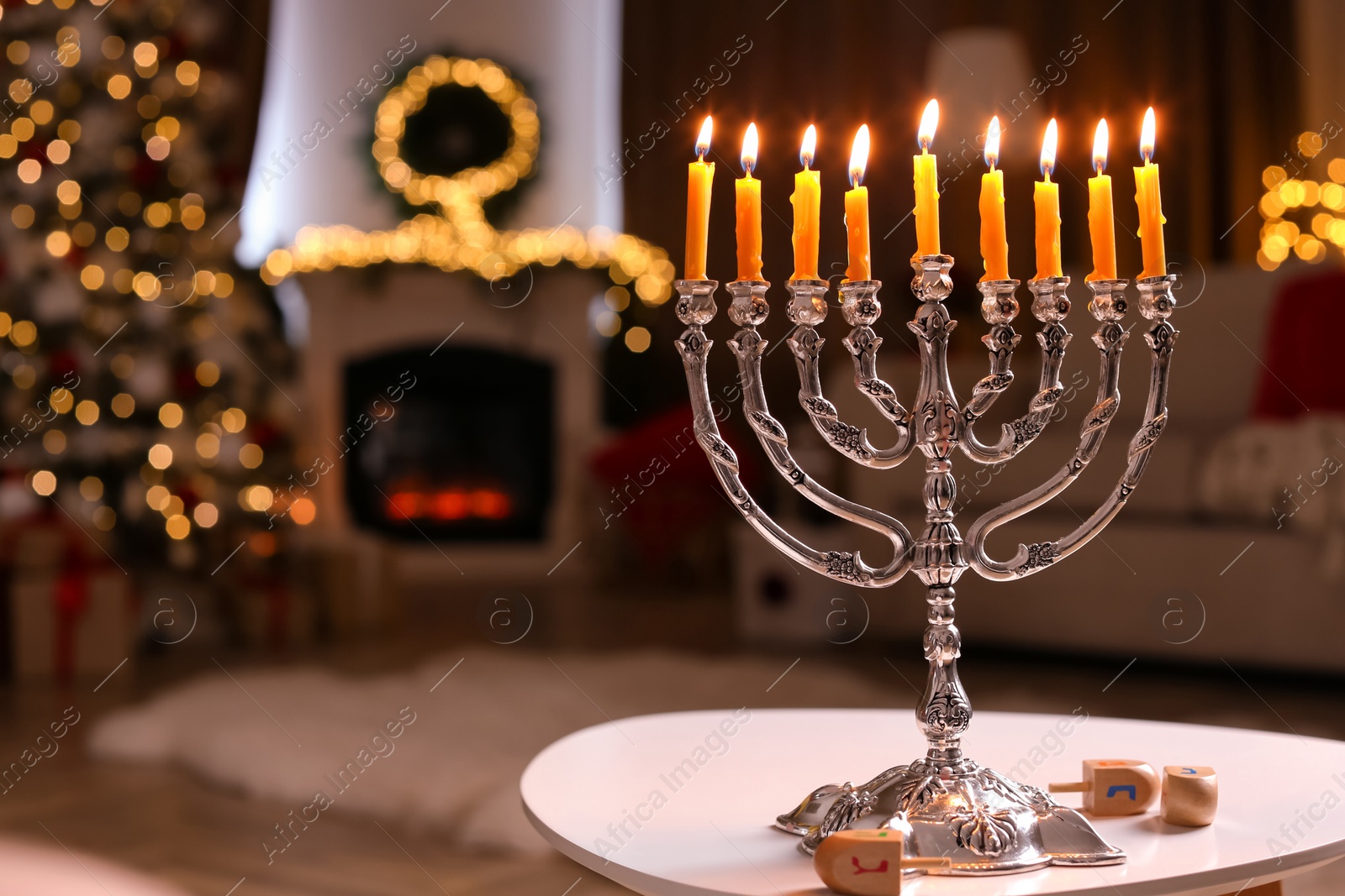 Photo of Silver menorah near dreidels with symbols He, Pe, Nun, Gimel on white table in room, space for text