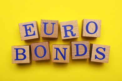 Photo of Word Eurobonds made of wooden cubes with letters on yellow background, flat lay