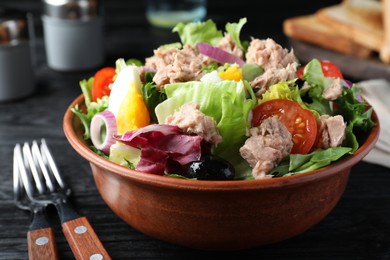 Photo of Bowl of delicious salad with canned tuna and vegetables served on black wooden table, closeup