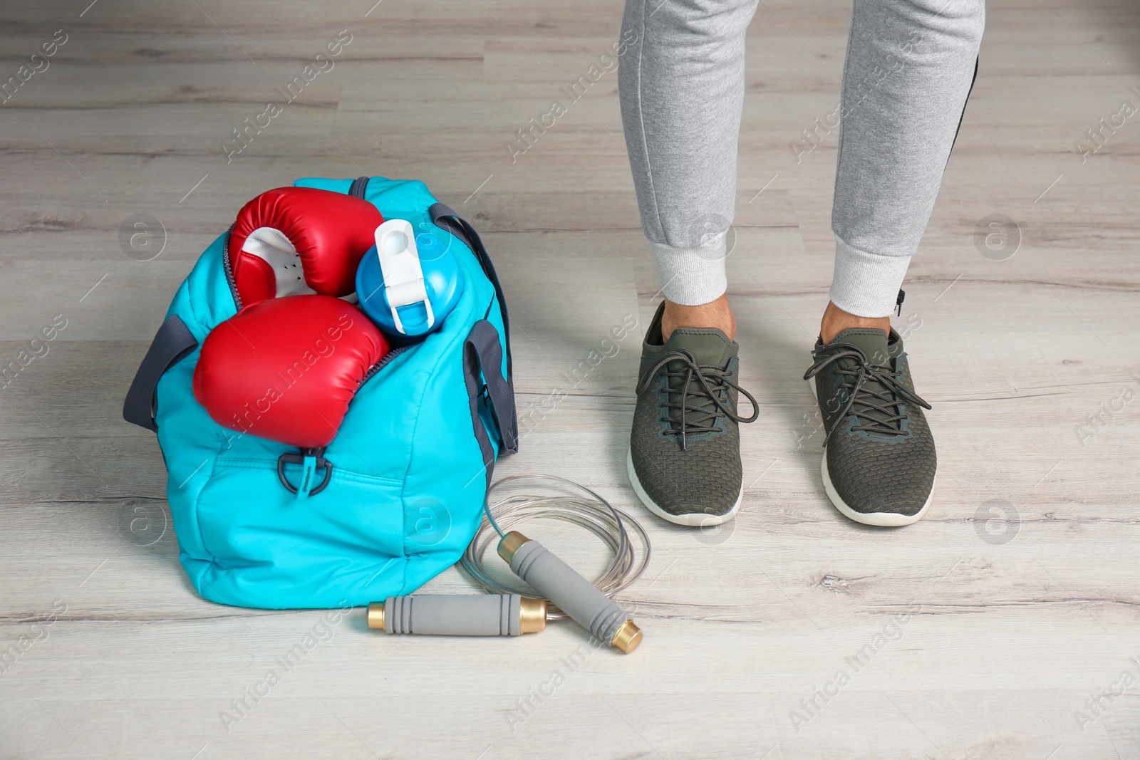 Photo of Young man in sportswear and bag with gym equipment indoors