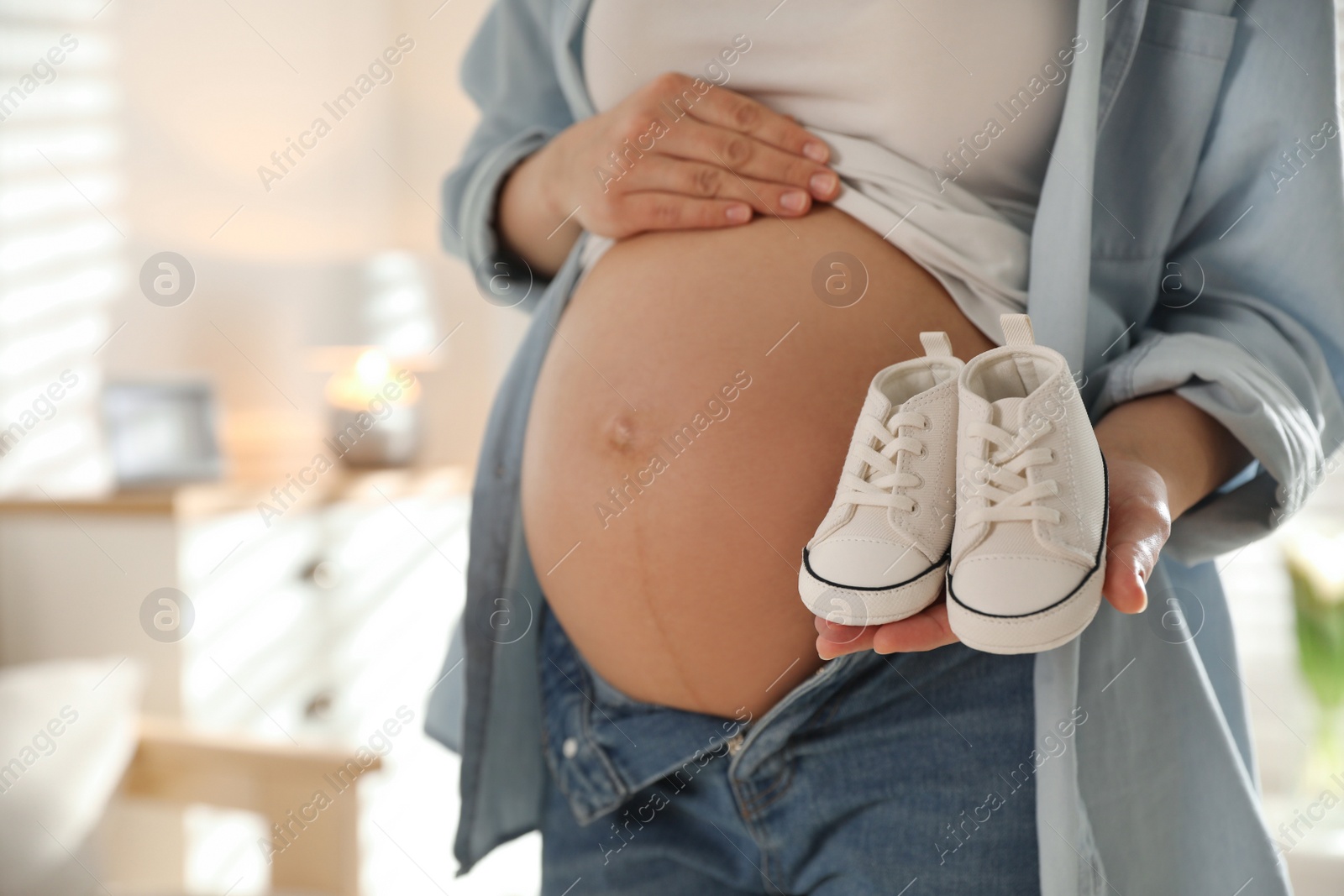 Photo of Young pregnant woman with baby's shoes indoors, closeup. Space for text