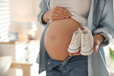 Young pregnant woman with baby's shoes indoors, closeup. Space for text