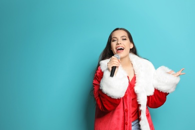 Photo of Young woman in Santa costume singing into microphone on color background. Christmas music