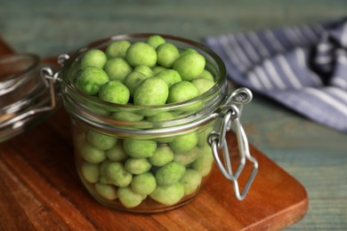 Photo of Tasty wasabi coated peanuts in glass jar on wooden table, closeup