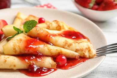 Delicious thin pancakes with strawberries and jam on table, closeup