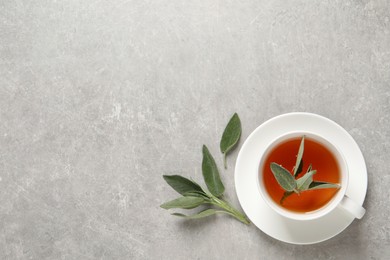 Photo of Cup of aromatic sage tea and fresh leaves on grey table, flat lay. Space for text