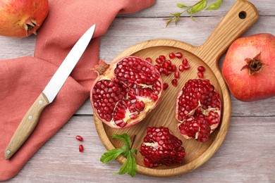 Fresh pomegranates, green leaves and knife on wooden table, flat lay