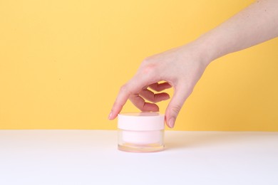 Woman with jar of cream on yellow background, closeup