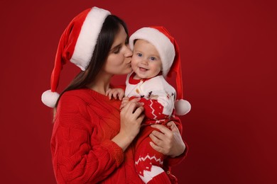 Happy mother with cute baby in Christmas outfits and Santa hats on red background