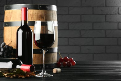 Photo of Delicious wine, wooden barrel and fresh grapes on black table, space for text