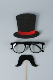 Fake mustache with party prop, paper hat and glasses on grey background, top view