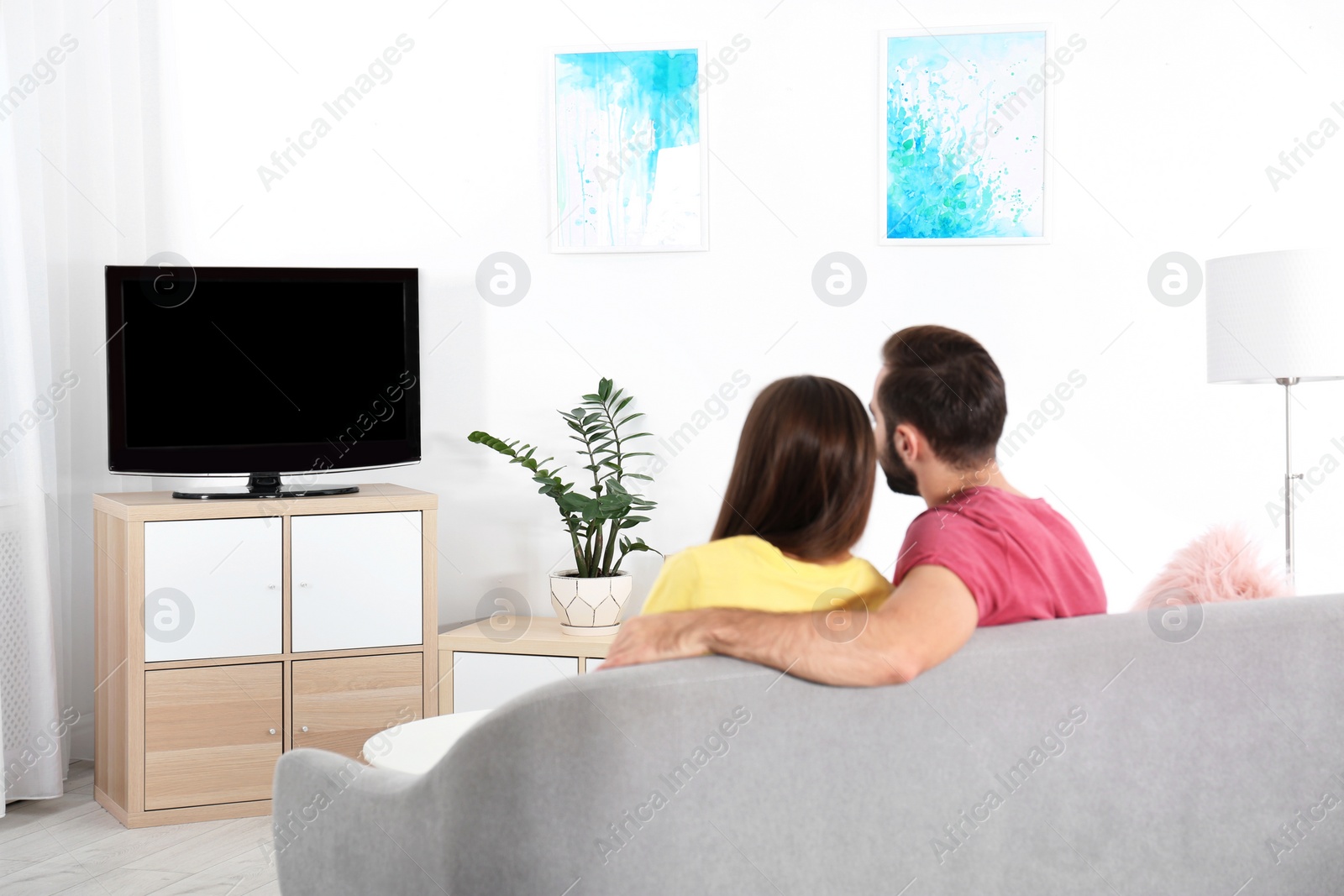 Photo of Young couple watching TV on sofa at home