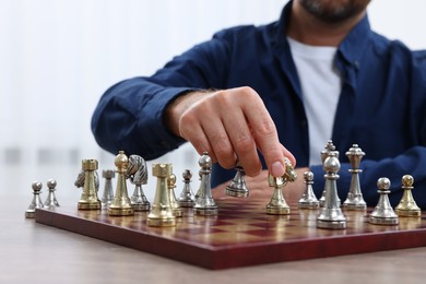 Photo of Man moving knight on chessboard at table indoors, closeup
