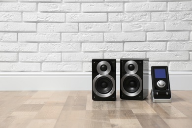 Photo of Modern powerful audio speakers and remote on floor near white brick wall. Space for text