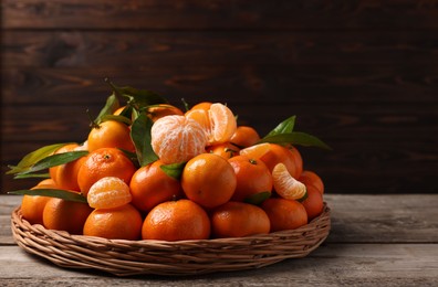 Fresh ripe juicy tangerines and green leaves on wooden table, space for text