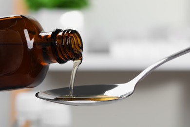 Pouring syrup from bottle into spoon against blurred background, closeup. Cold medicine