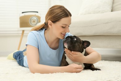 Photo of Happy woman hugging cute French Bulldog on soft carpet in room