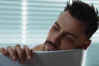 Upset man thinking about something in bathtub at home, closeup. Loneliness concept