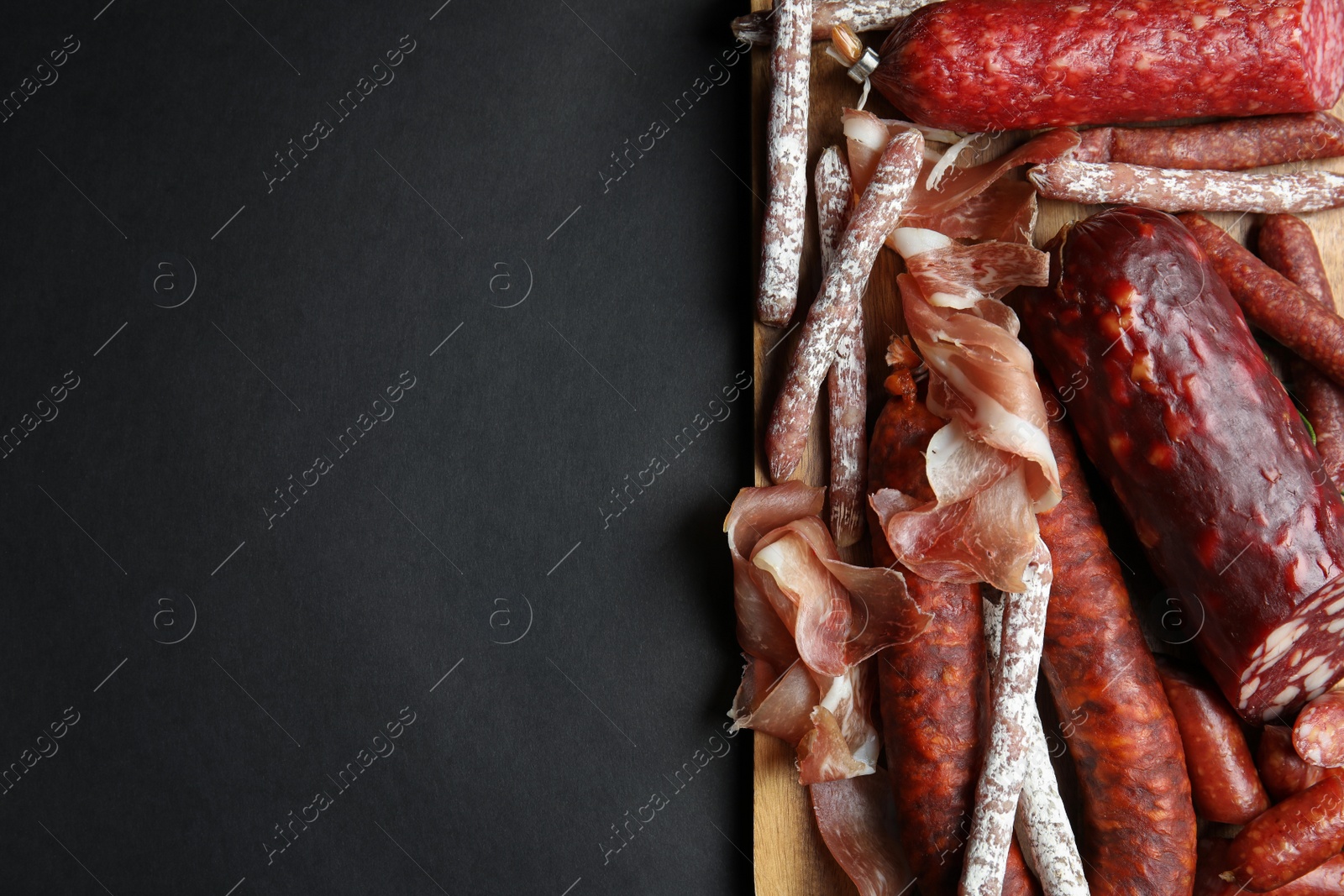 Photo of Different types of sausages served on black background, top view. Space for text