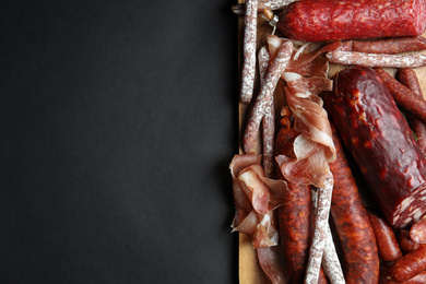 Photo of Different types of sausages served on black background, top view. Space for text