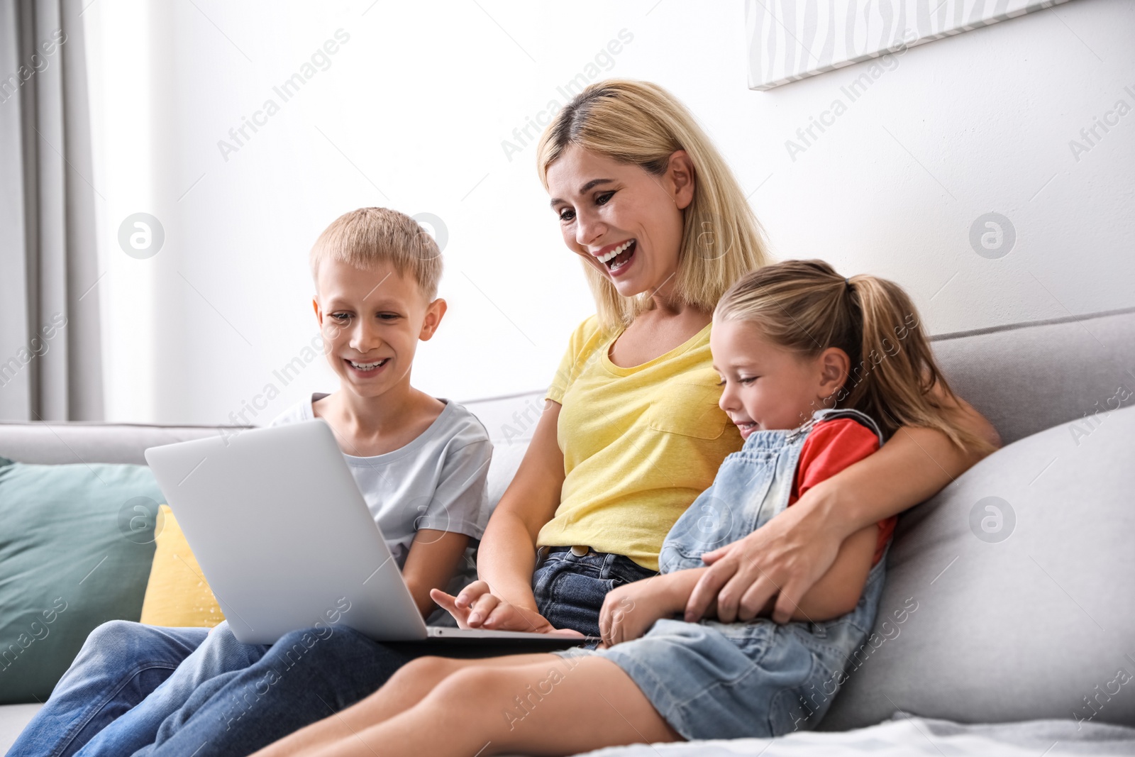 Photo of Happy mother using laptop with her children on sofa at home