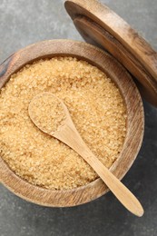 Brown sugar in bowl and spoon on grey textured table, top view