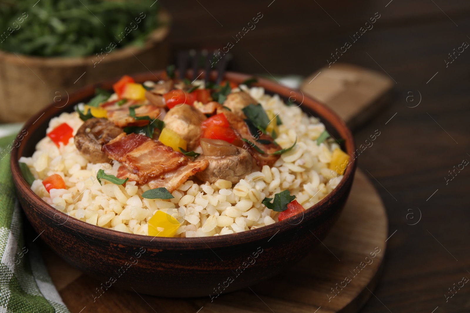 Photo of Cooked bulgur with vegetables, fried bacon and mushrooms in bowl on wooden table, closeup. Space for text