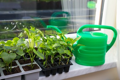 Photo of Seedlings growing in plastic containers with soil and watering can on windowsill indoors