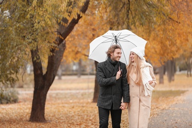 Photo of Romantic couple with umbrella walking in park on autumn day