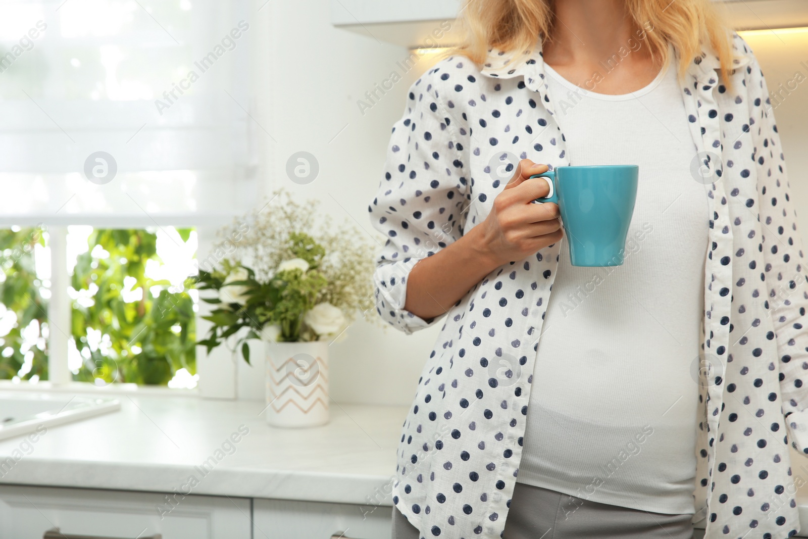 Photo of Beautiful pregnant woman drinking tea in kitchen, closeup