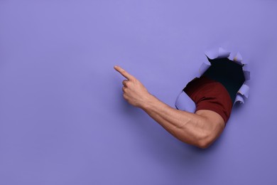 Photo of Special promotion. Man pointing at something through hole in purple paper, closeup. Space for text