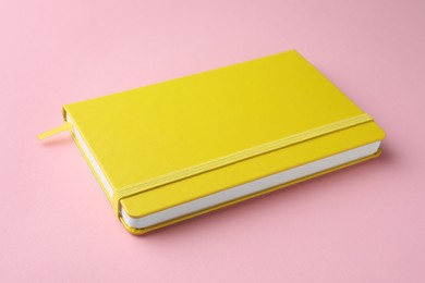 Photo of Closed notebook with blank yellow cover on light pink background