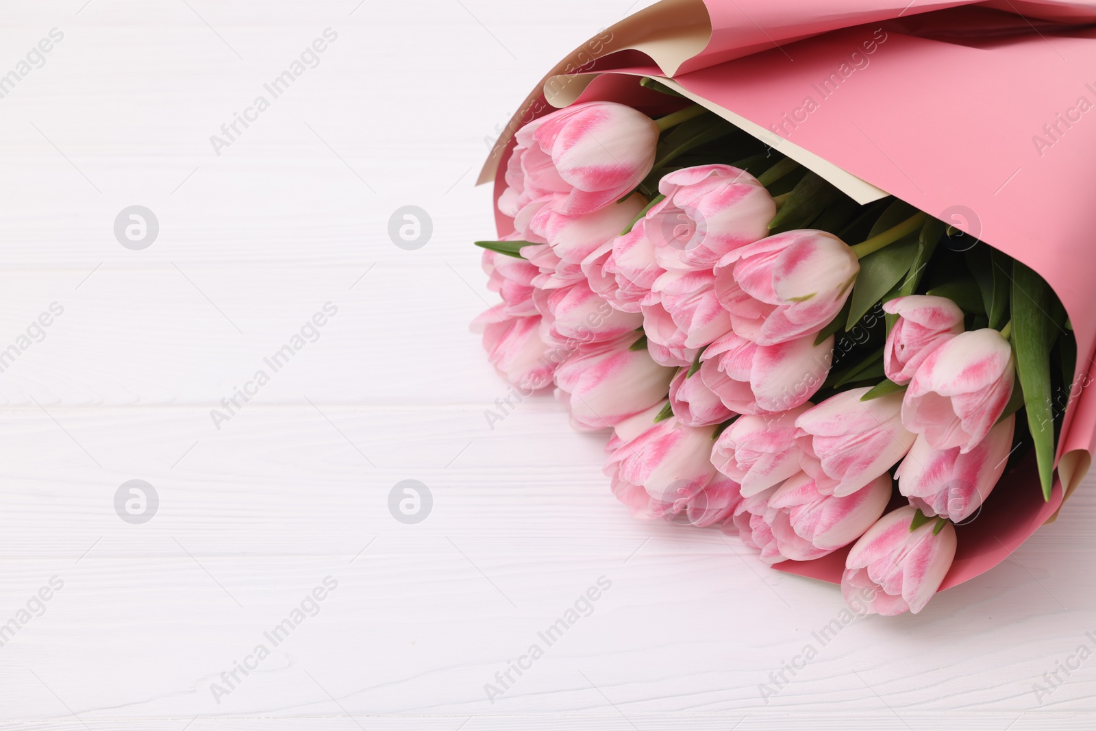 Photo of Beautiful bouquet of fresh pink tulips on white wooden table. Space for text