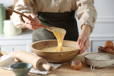 Photo of Woman kneading dough with spoon in bowl at wooden table in kitchen, closeup