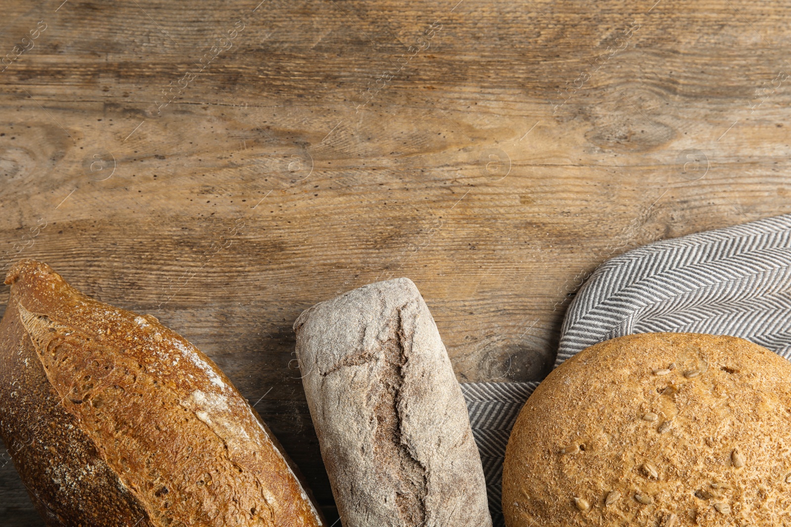 Photo of Loaves of different breads on wooden background, flat lay. Space for text