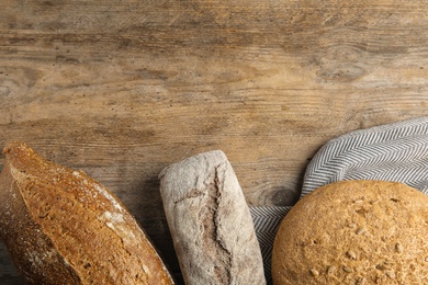 Photo of Loaves of different breads on wooden background, flat lay. Space for text