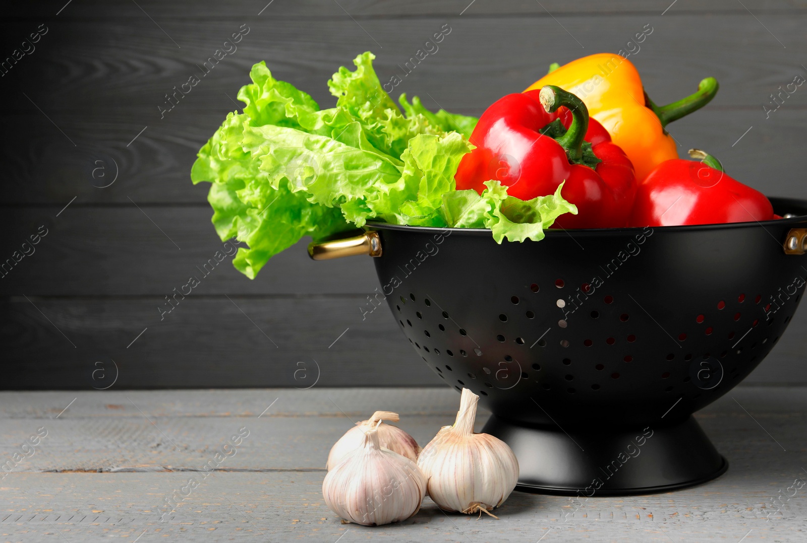 Photo of Black colander and different vegetables on rustic wooden table. Space for text