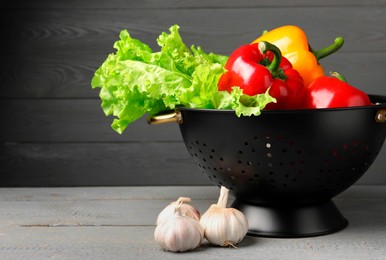 Photo of Black colander and different vegetables on rustic wooden table. Space for text