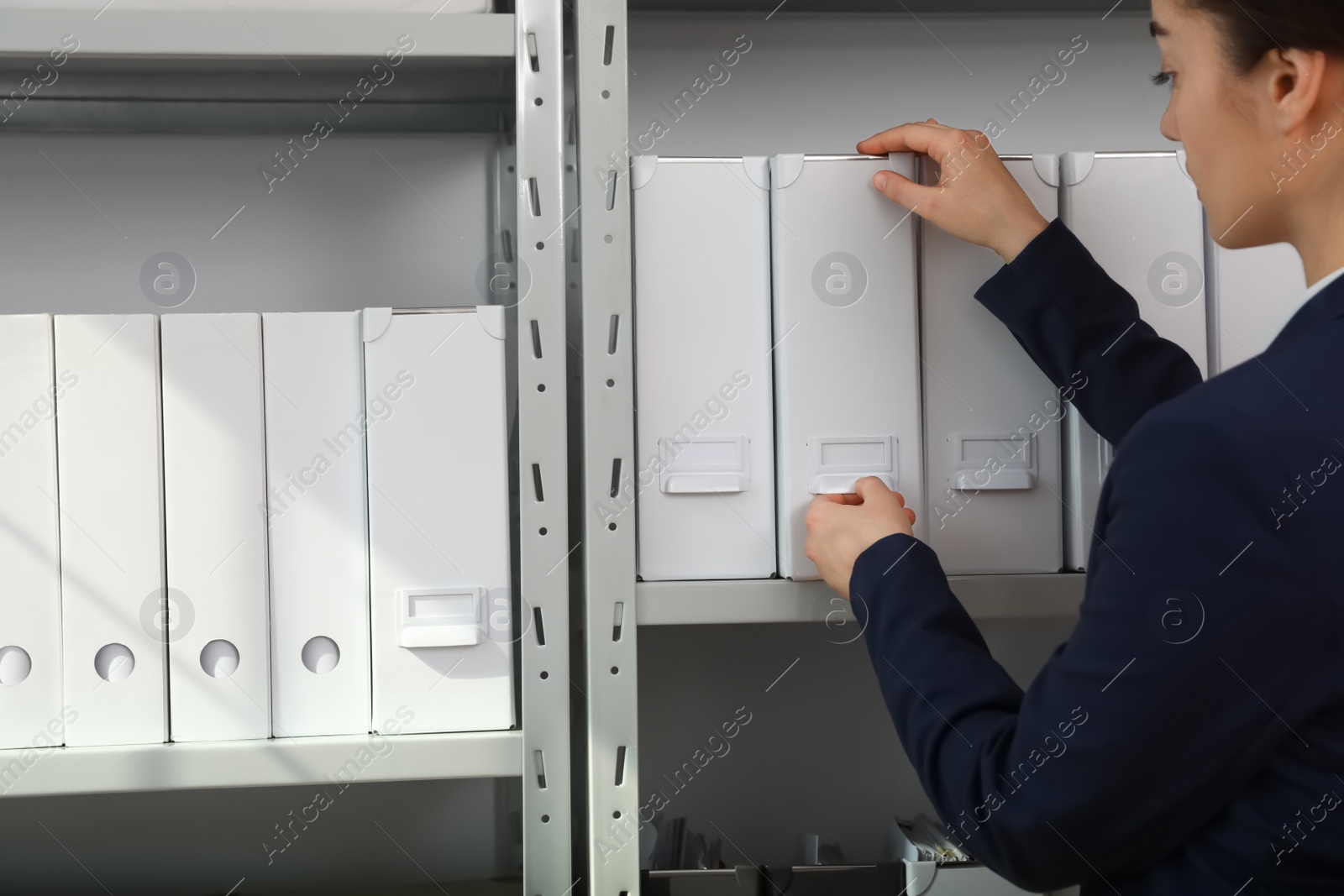 Photo of Woman taking folder with documents from shelf in archive