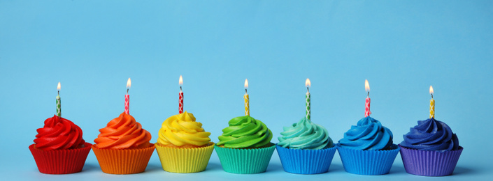 Photo of Delicious birthday cupcakes with burning candles on light blue background