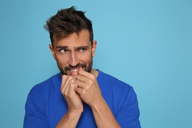 Man biting his nails on light blue background. Space for text
