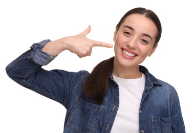 Young woman pointing at her clean teeth and smiling on white background