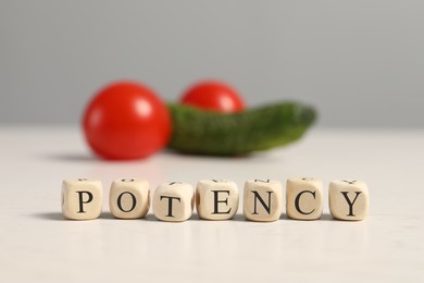 Photo of Cubes with word Potency near cucumber and tomatoes symbolizing male genitals on white wooden table